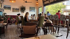 A restaurant interior with tables, chairs, hanging lights, ceiling fans, and artwork on the walls.