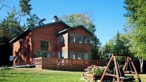 A log cabin with a deck, surrounded by a grassy yard and trees. - Aerie - Vermilion Dam Lodge (Orr)