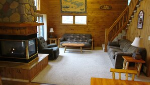 A cozy cabin interior with a stone fireplace, wooden walls, a couch, and a staircase. - Aerie - Vermilion Dam Lodge (Orr)