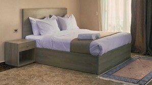 Een slaapkamer met een bed, nachtkastje, airconditioning en een raam met gordijnen.