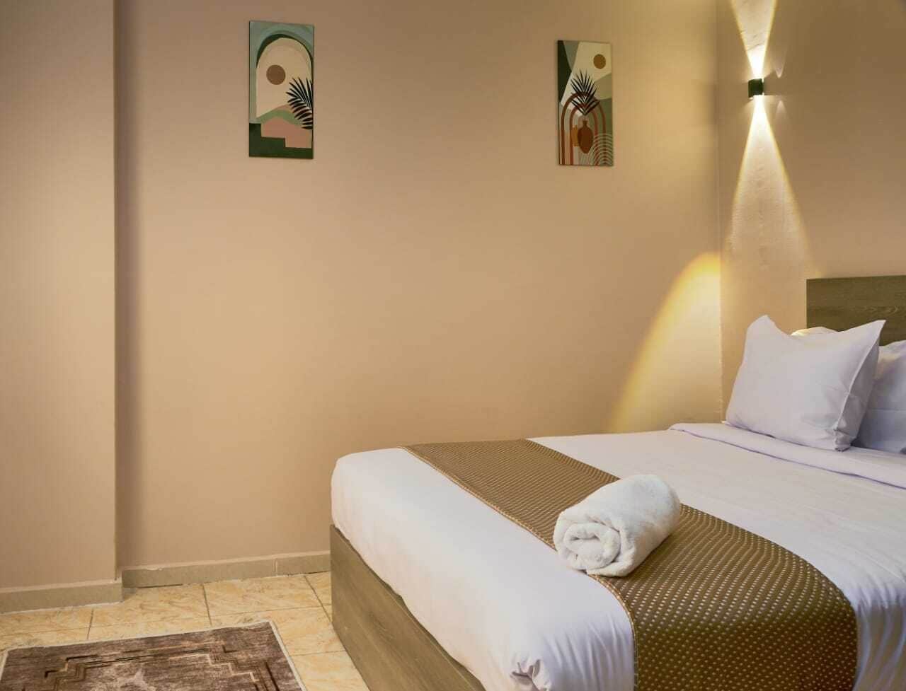 Une chambre d’hôtel avec un lit parfaitement fait, une lampe fixée au mur et deux tableaux abstraits.