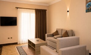A modern living room with a sofa, a coffee table, and a flat-screen TV mounted on the wall. - Roadhouse New Cairo Residence (New Cairo)