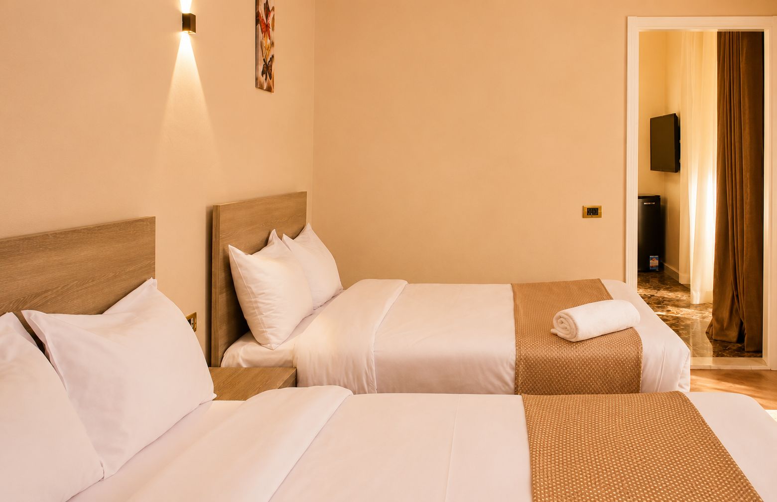 A hotel room with two beds, a wooden headboard, a wall-mounted TV, and a door leading to a bathroom.