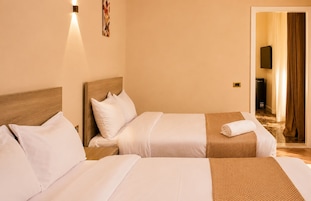 A hotel room with two beds, a wooden headboard, a wall-mounted TV, and a door leading to a bathroom.