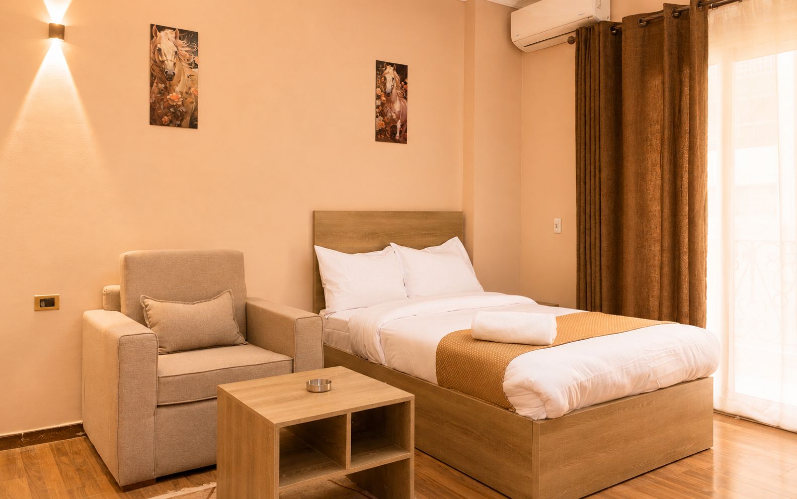 A hotel room with a bed, a sofa, a bedside table, and two wall-mounted artworks.