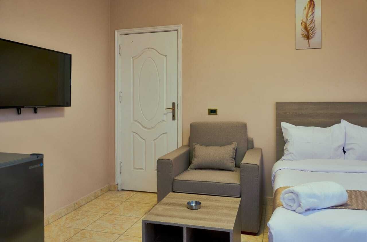 Habitación de hotel con cama, sofá, una mesita con un bol, televisor y puerta.