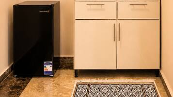 A compact kitchenette with a refrigerator, microwave, and a small countertop with a kettle and cups.