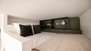 Un dormitorio con cama, almohadas, una estantería con objetos decorativos y un cabecero blanco.