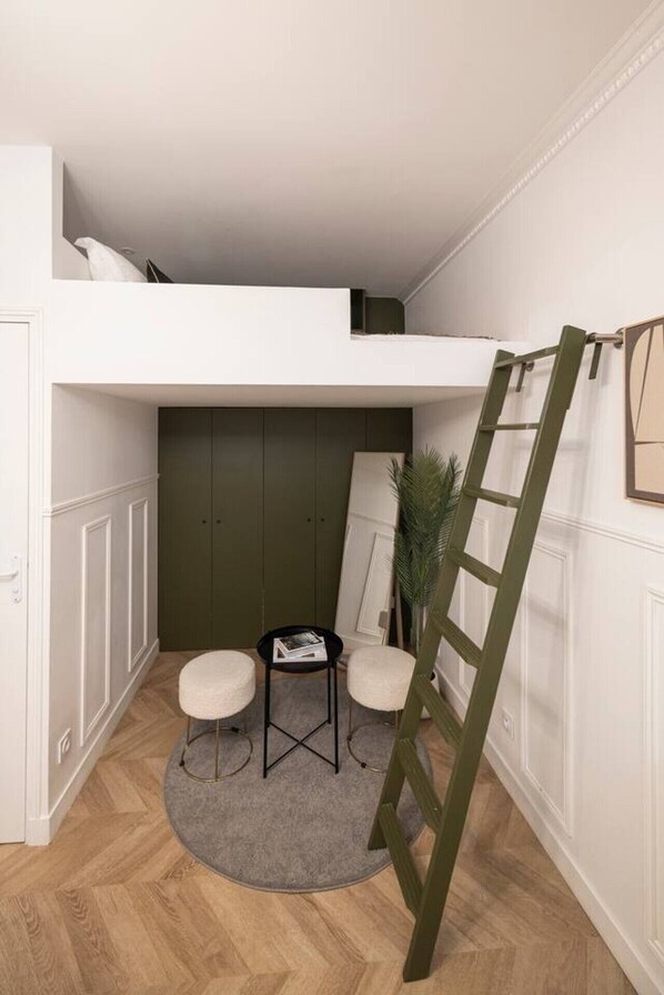 Un dormitorio tipo loft con una cama litera, una mesita pequeña con dos sillas, una escalera y una planta en maceta.