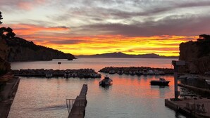A coastal marina at sunset with boats docked, a pier, and rocky cliffs in the background.