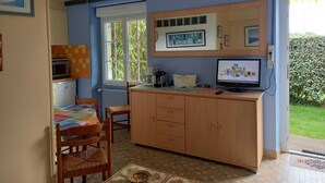 A compact kitchen with a microwave, toaster, and a television on a wooden cabinet. There is a dining table with chairs and a window with a view of greenery. - 54 m2 apartment 150m from the sea (main beach) and 100m from the village (Damgan)
