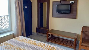 Una habitación de hotel con cama, televisor montado en la pared, un banco de madera y una puerta.