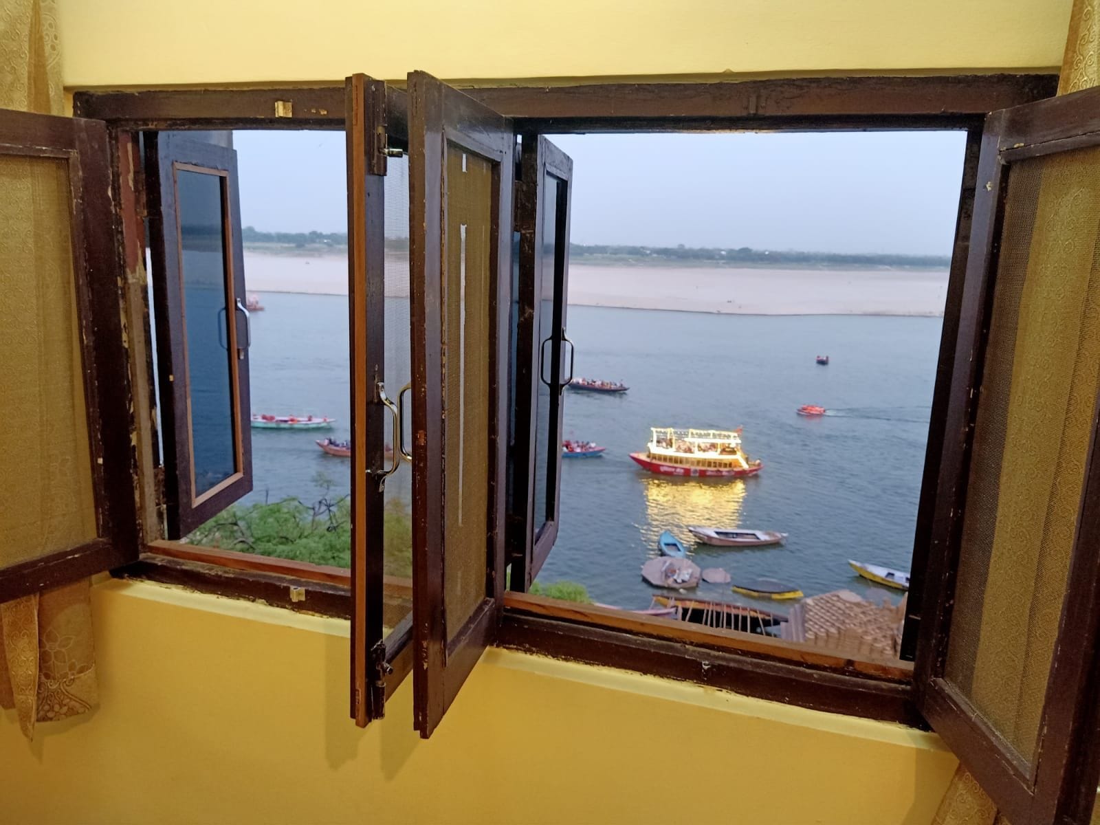 Vista a través de una ventana abierta que muestra un río y barcos.