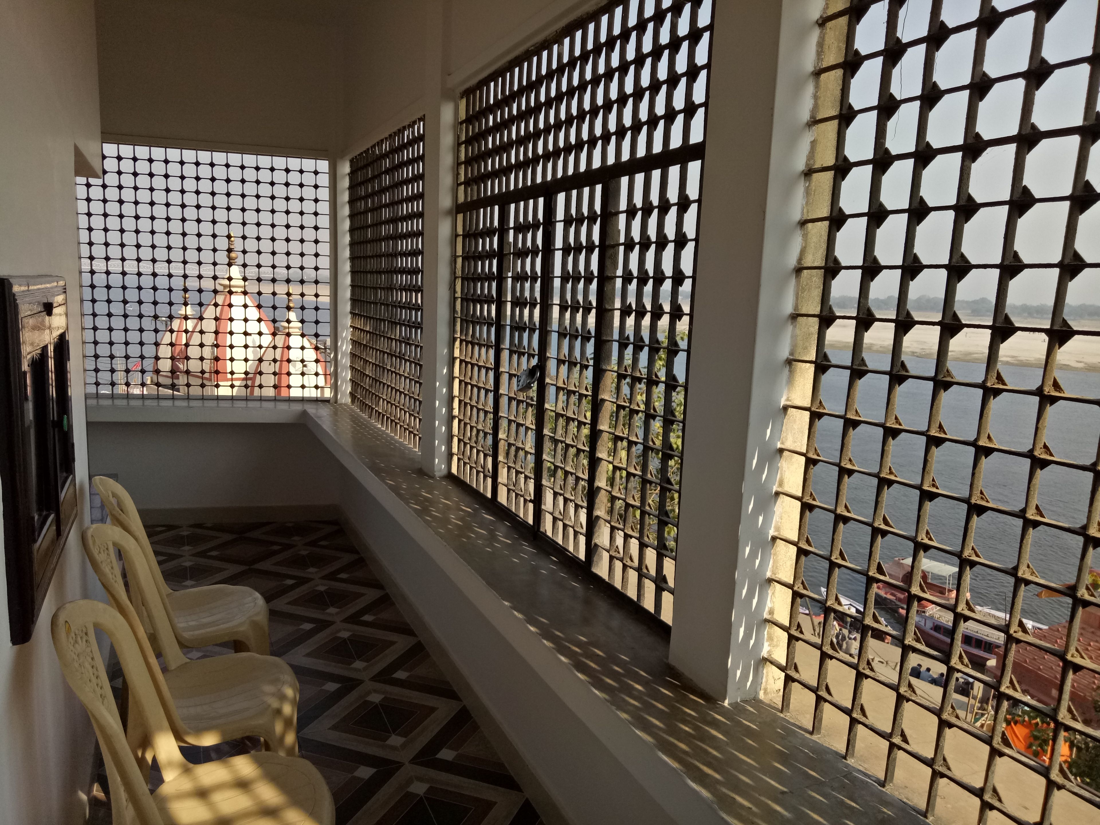 A balcony with a view of a river, a tiled floor, and a row of plastic chairs.