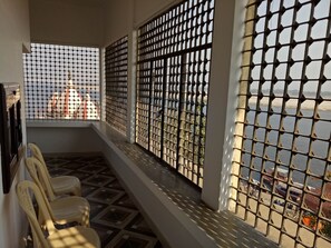 A balcony with a view of a river, a tiled floor, and a row of plastic chairs. - Scindhia Guest House (Varanasi)