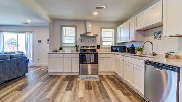A modern kitchen with white cabinets, stainless steel appliances, and a wooden floor.
