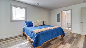 A bedroom with a large bed, a window, and a door leading to another room.