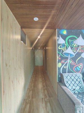 A hallway with wooden paneling, a patterned floor, and a colorful mural on the right wall. - Bodh Niwas - Unit of Nest Community (Manali)