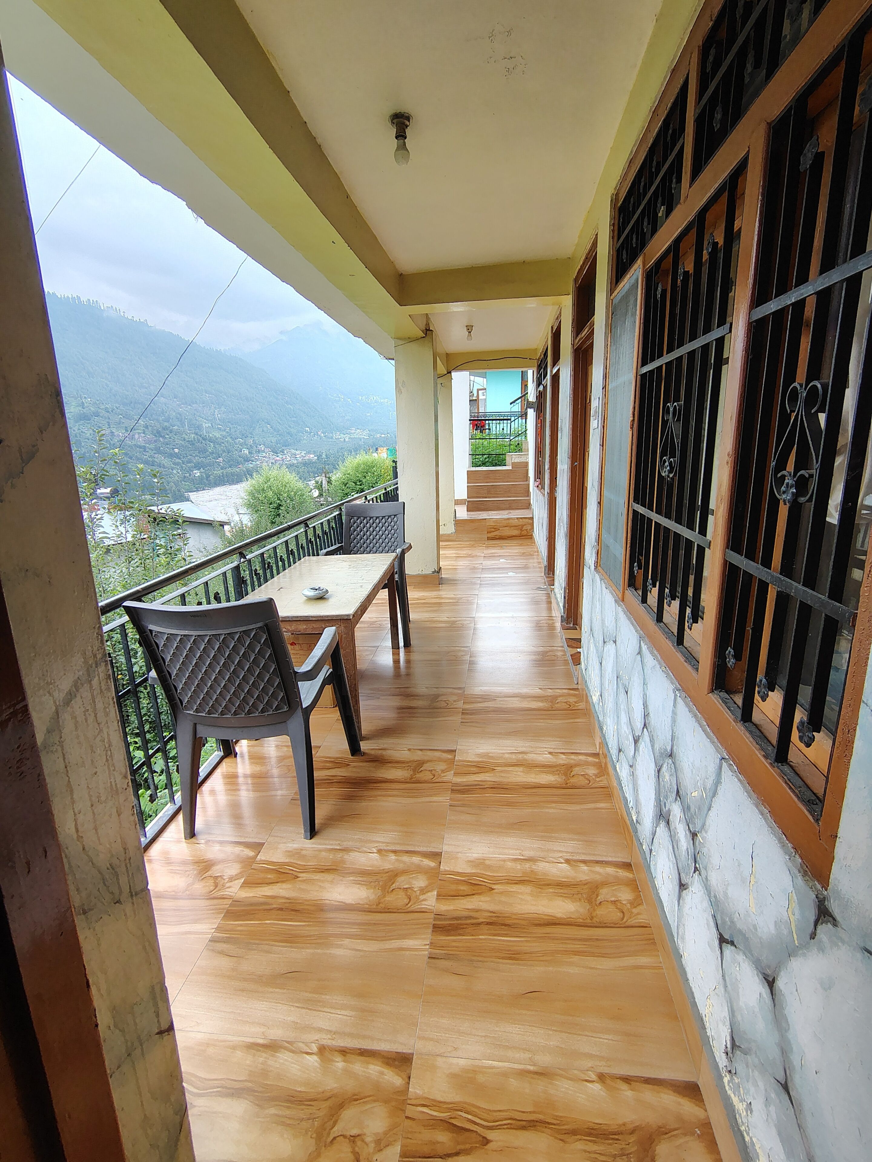 A balcony with a table and chairs, a view of mountains, and a staircase leading to an upper level.