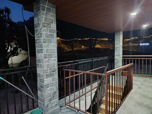 A covered outdoor area with a stone pillar, a metal railing, and a staircase. - Bodh Niwas - Unit of Nest Community (Manali)