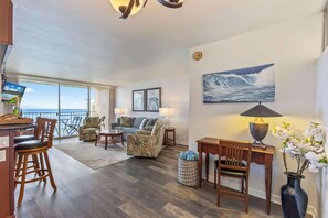 A spacious living area with a large window overlooking the ocean, a sofa, a coffee table, and a lamp.