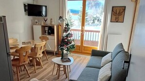 Un salón acogedor con un sofá gris, sillas de madera, una mesita con un árbol de Navidad y un televisor montado en la pared.