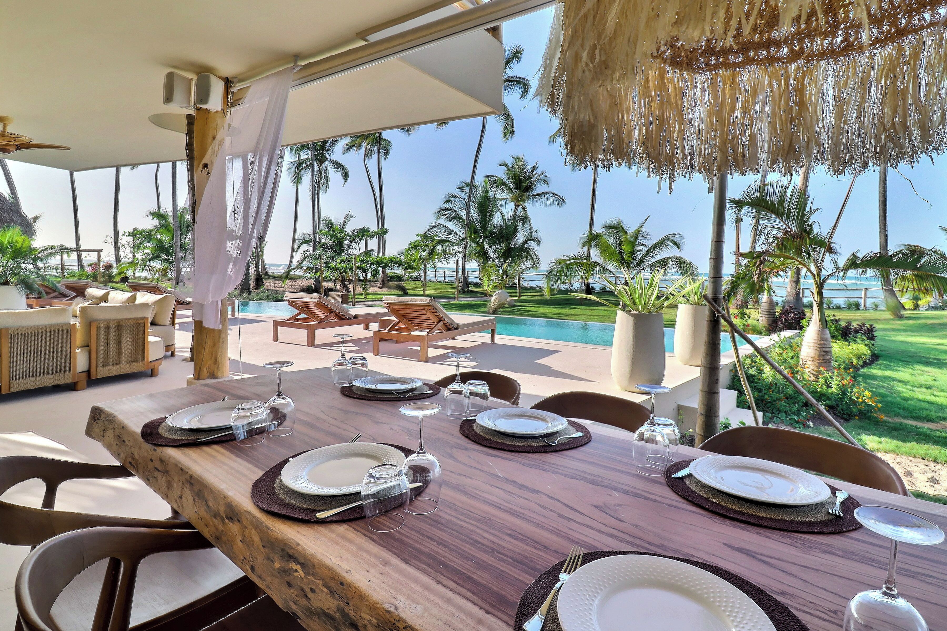 A dining area with a wooden table set for a meal, overlooking a pool and palm trees.