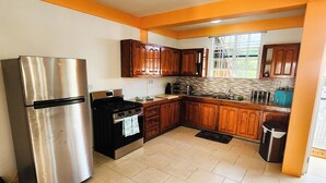 A kitchen with a stainless steel refrigerator, wooden cabinets, a tiled backsplash, and a window with a view of greenery. - Elite Island Breeze 2-bed apt in Jimmit, WiFi, AC, Free Parking,Central location (Jimmit)
