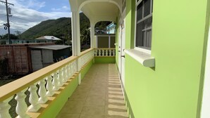 A covered balcony with a tiled floor, white balustrade, and a green wall. - Elite Island Breeze 2-bed apt in Jimmit, WiFi, AC, Free Parking,Central location (Jimmit)