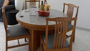 A dining area with a round table, four wooden chairs, a vase, and a framed painting of a beach pathway.