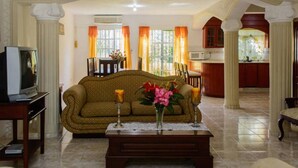 A living room with a sofa, coffee table, and a TV. There is a kitchen in the background with cabinets and a window. - 4-bedroom luxury villa in tranquil Puerto Plata with WiFi, AC stunning rooftop (Puerto Plata)