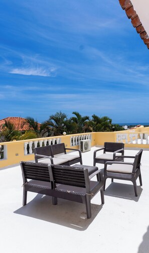 Una terraza en la azotea con mobiliario exterior, cielo despejado y vista al mar.