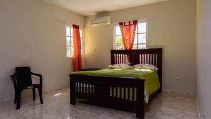A bedroom with a bed, a chair, and two windows with curtains. - 4-bedroom luxury villa in tranquil Puerto Plata with WiFi, AC stunning rooftop (Puerto Plata)