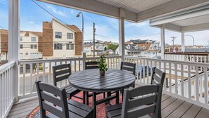 Un espace extérieur abrité, doté d’une table ronde et de chaises, d’une plante en pot et offrant une vue sur des immeubles d’habitation.