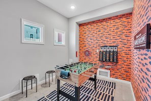 Una habitación con una mesa de fútbol de mesa, dos taburetes, un televisor montado en la pared y un diseño de peces en la pared.
