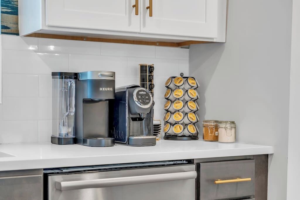 A kitchen with a coffee maker, a coffee grinder, and a container of coffee pods.