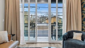 Een woonkamer met een schuifdeur naar een balkon, een bank, een fauteuil en een kleine tafel.