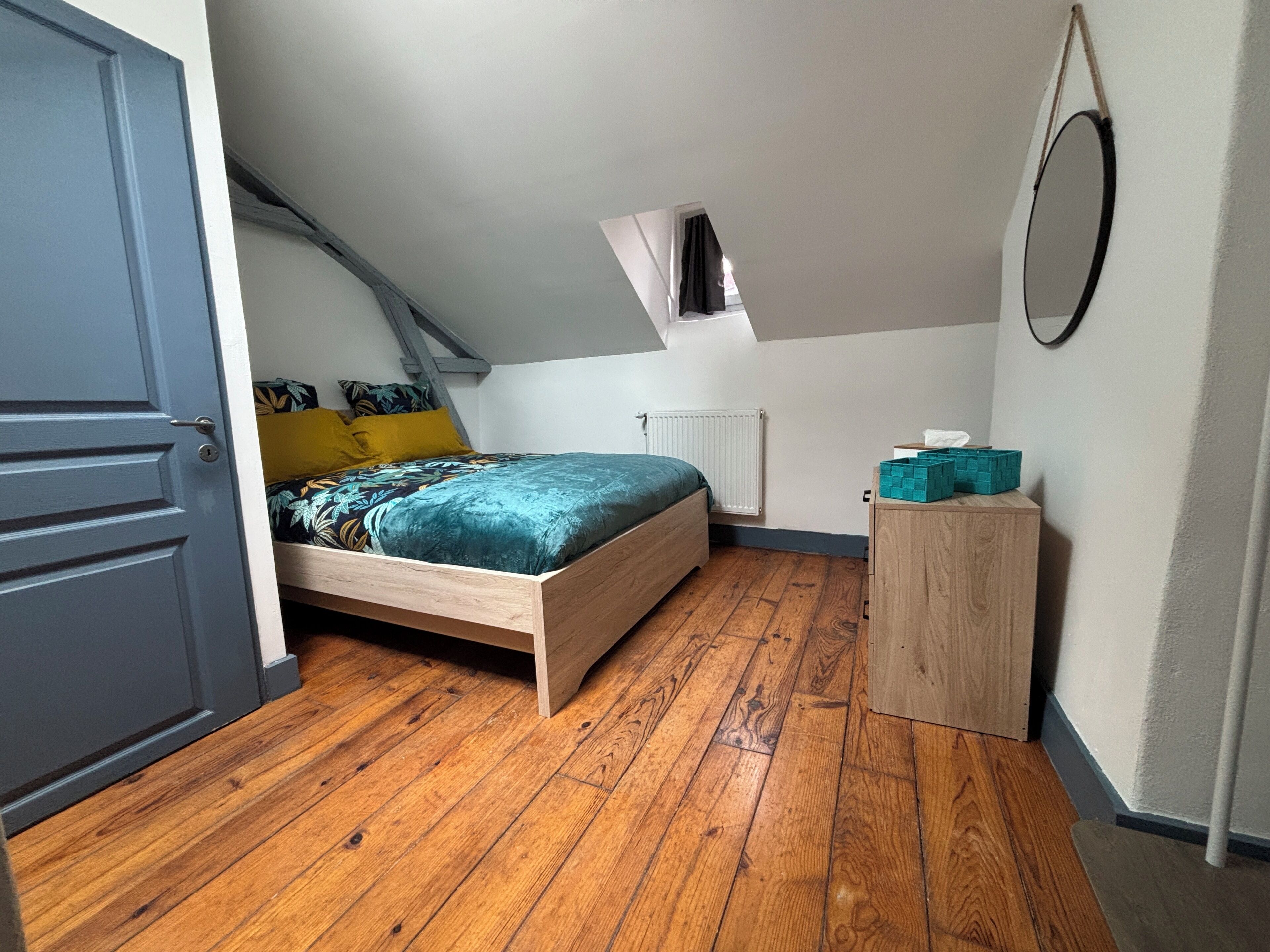 A bedroom with a sloped ceiling, a bed with a floral bedspread, a wooden cabinet, and a small window.