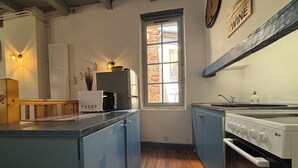A compact kitchen with a stove, microwave, and cabinets. There's a window with a view of a brick building outside. - Pretty house in the historic district of Cahors close to shops (Cahors)