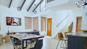 Cocina moderna con zona de comedor, que incluye una isla grande, taburetes de bar y un televisor en la pared.