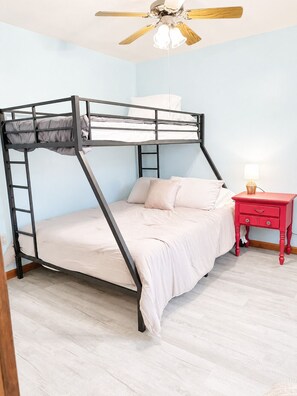 Un lit superposé avec une échelle, une table de chevet avec une lampe et un ventilateur de plafond.