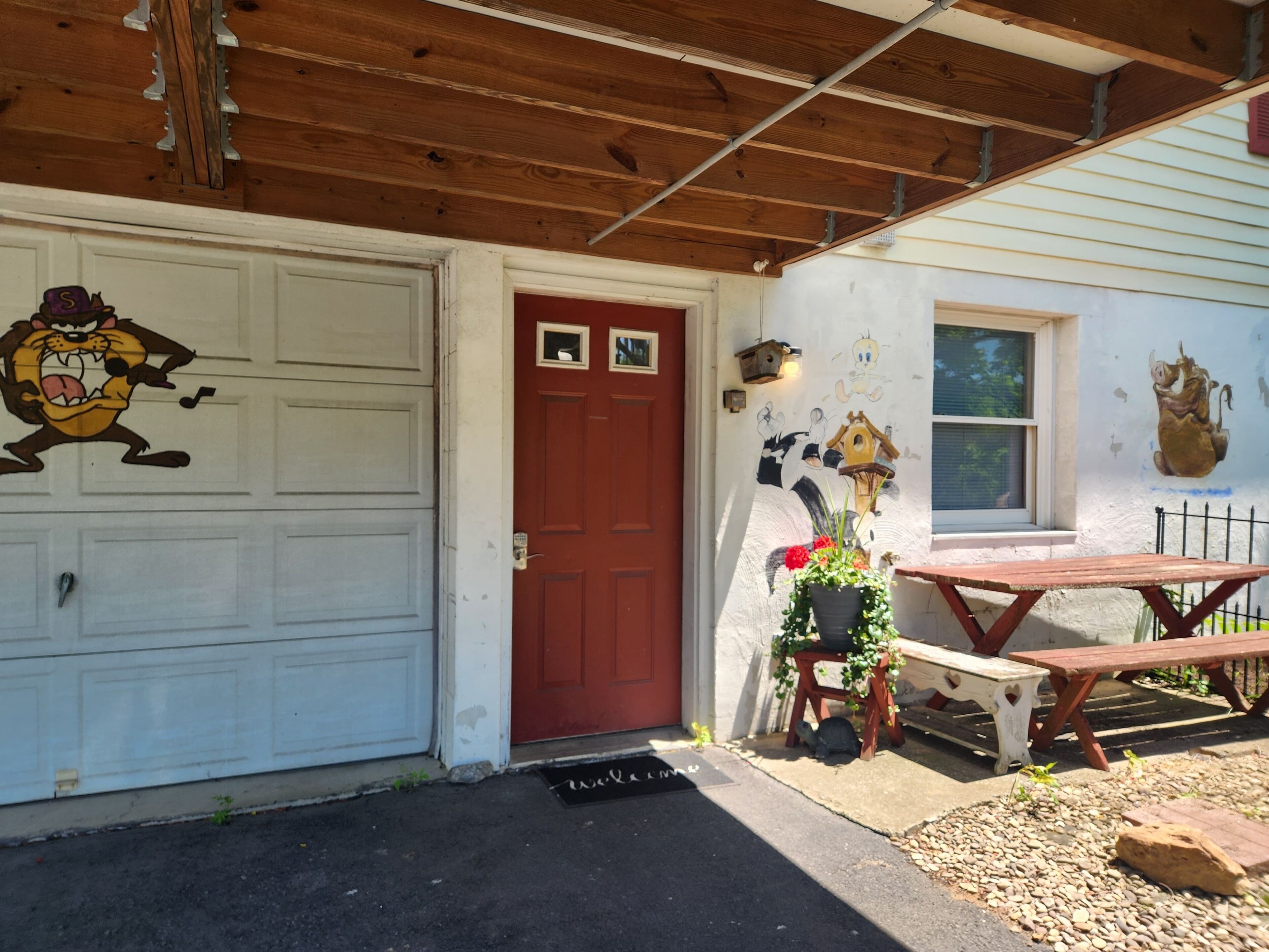 Una casa con garage, una porta rossa, una panchina e un tavolo all'esterno.