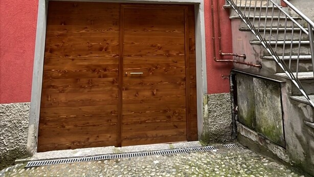 Un bâtiment rouge avec une porte de garage en bois, un escalier en métal et un sol pavé de pierres.