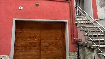 Un edificio rojo con una puerta de garaje de madera, una escalera de metal y un suelo de piedra.