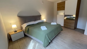 Un lit bien fait, recouvert d’une couverture verte, avec une lampe de chevet et une table de nuit en bois.