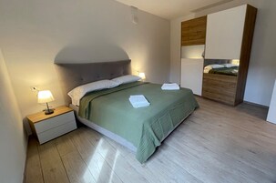 Una cama bien hecha con una colcha verde, una lámpara de noche y una mesita de madera.