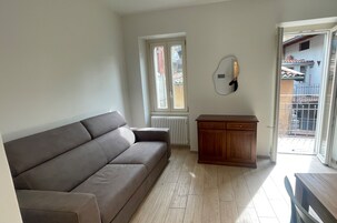 Una sala de estar con un sofá, un mueble de madera y un ventanal corredero que da a un espacio exterior.