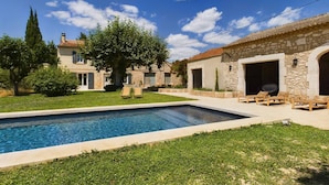 A pool area with a clear blue pool, surrounded by a well-maintained lawn and a stone building with an open patio. - Mas Sainte Croix - Authentic renovated farmhouse in Provence with swimming pool (Fontvieille)