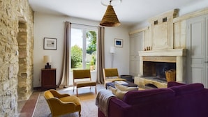 A living room with a stone wall, a fireplace, and a large window. - Mas Sainte Croix - Authentic renovated farmhouse in Provence with swimming pool (Fontvieille)