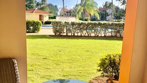 A patio with a round glass table and wicker chairs, overlooking a well-maintained lawn and palm trees.